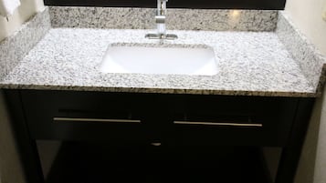 Casa de banho com bancada de granito, lavatório branco e espelho em cima.
