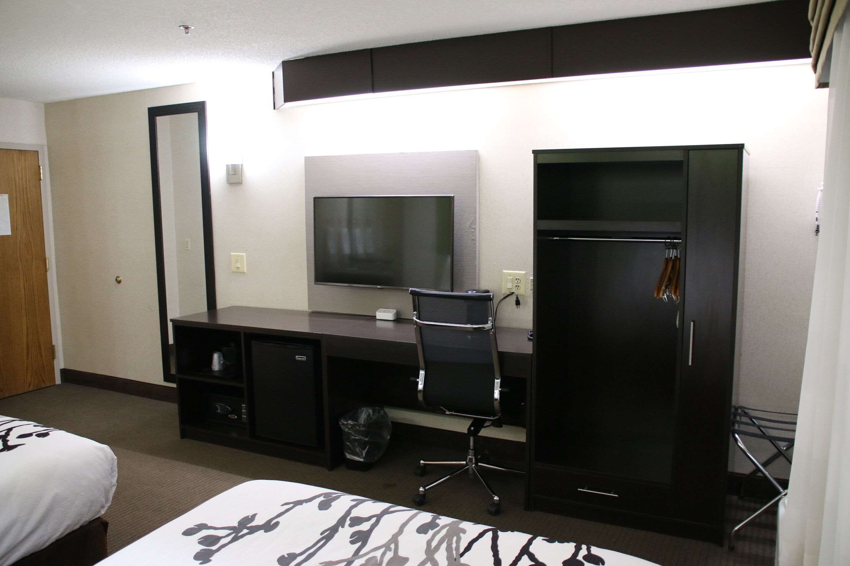 A hotel room with a bed, a desk with a chair, a TV, and a wardrobe.