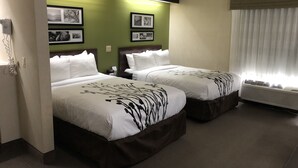 Ein Hotelzimmer mit zwei Betten, grünen Wänden, gerahmten Bildern, einem Nachttisch und einem Fenster mit Jalousien.