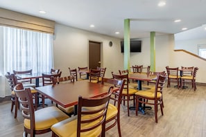 A dining area with multiple wooden tables and chairs, a clock on the wall, and a television mounted on the wall.