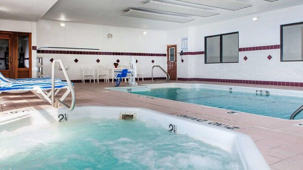 Un área de piscina interior con dos piscinas separadas, una con una sección de hidromasaje, y un espacio de descanso con sillas y una mesa.