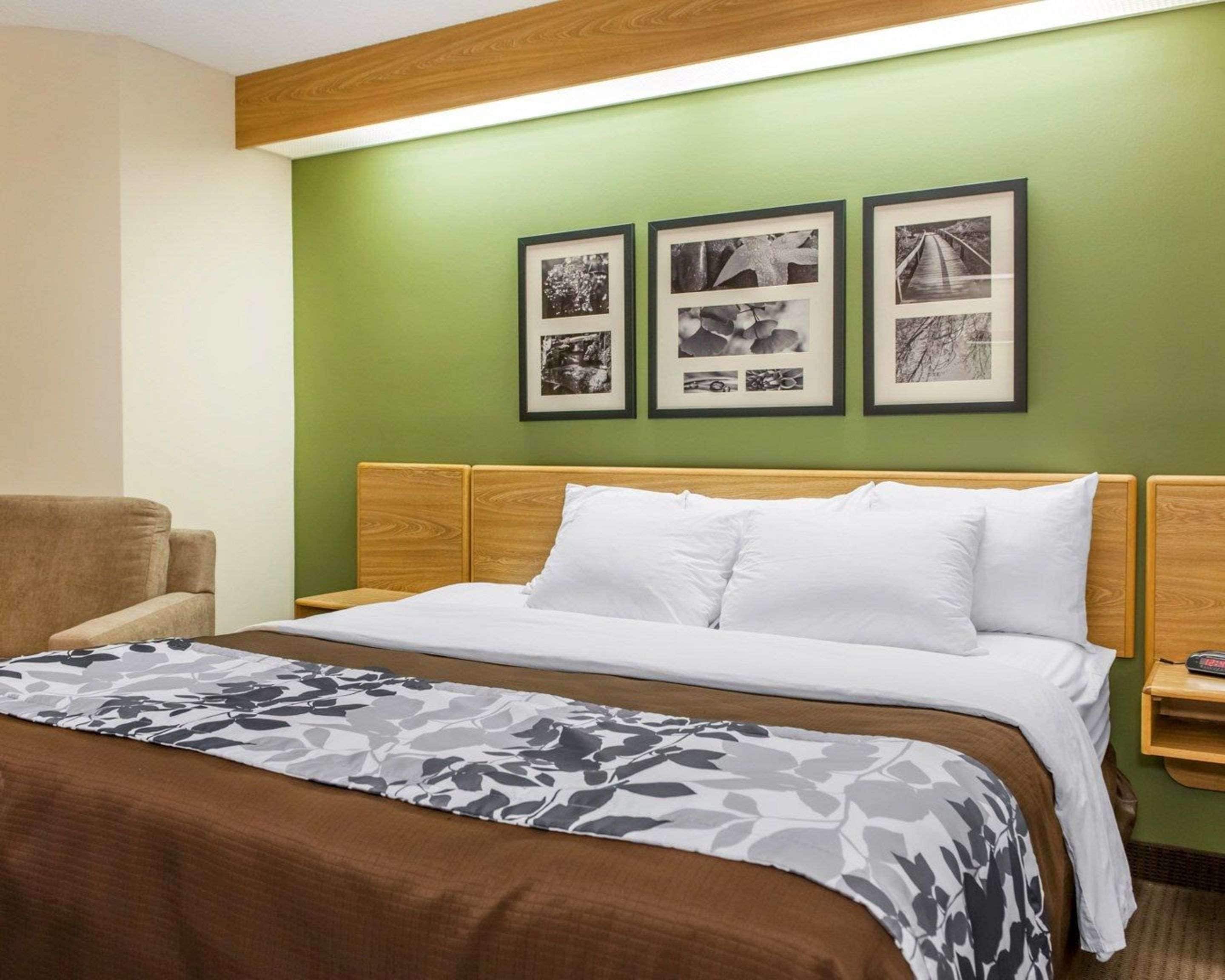 A hotel room with a wooden headboard, a bed with white bedding, a floral-patterned throw, and three framed photographs on the wall.