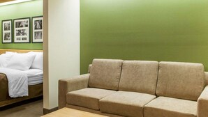 Una habitación con un sofá beige, una mesa de centro de madera y una cama con ropa de cama blanca.