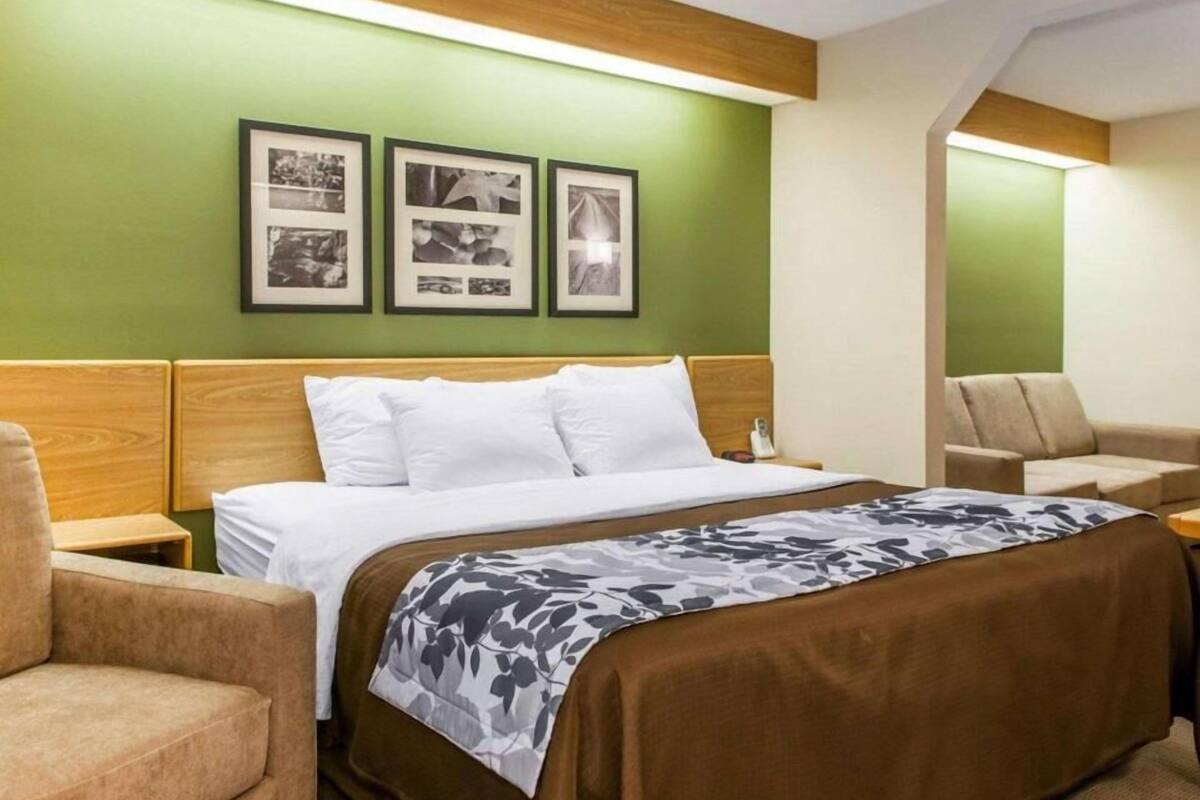 A hotel room with a bed, a nightstand, a chair, and a wall with framed pictures.