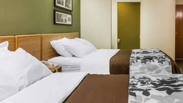 A hotel room with two beds, a wooden headboard, a bedside table with a phone, and framed pictures on the wall.