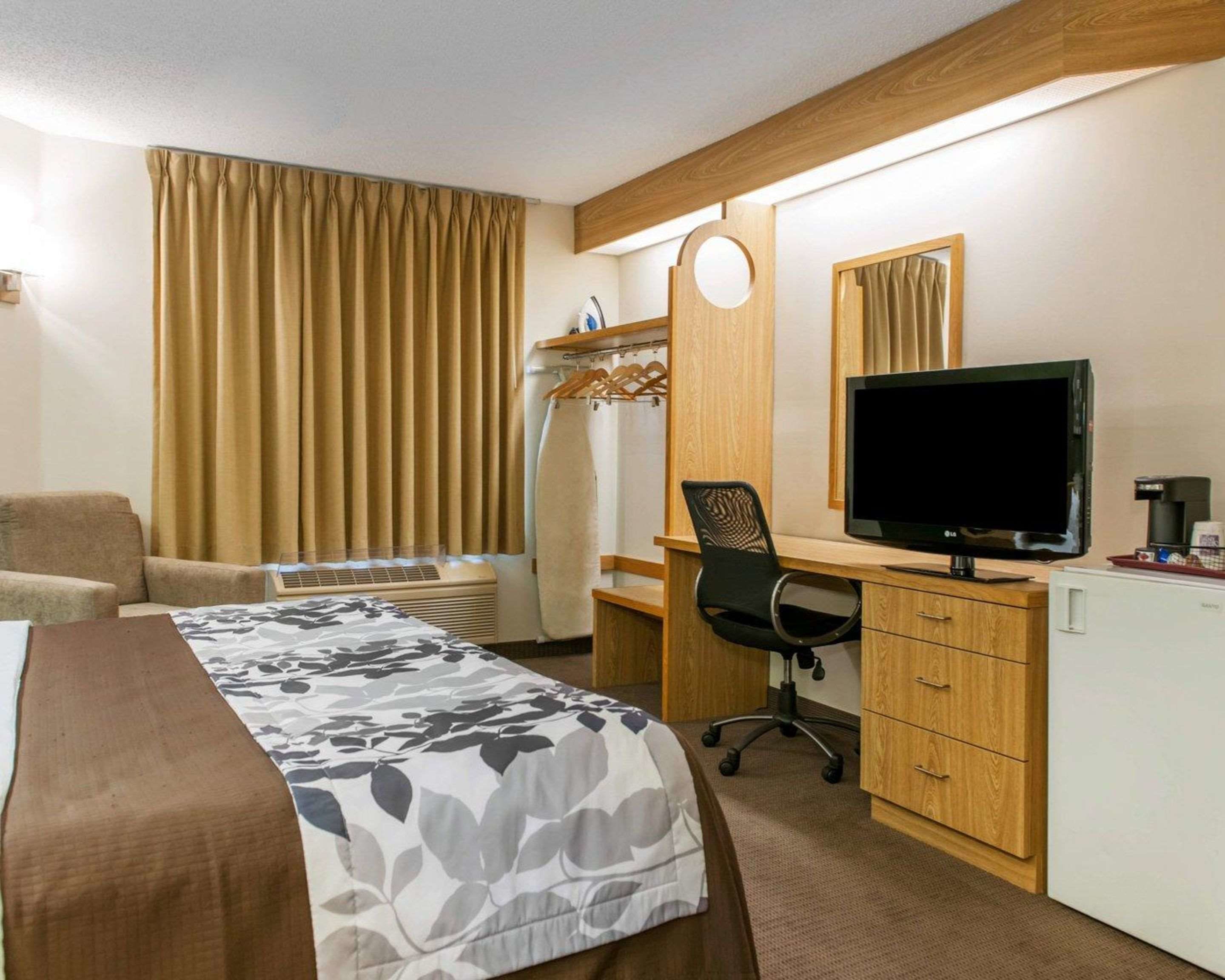 A hotel room with a bed, a desk with a computer, a chair, a TV, and a coffee machine.
