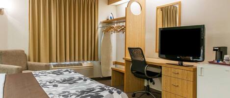 A hotel room with a bed, a desk with a computer, a chair, a TV, and a coffee machine.
