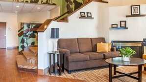 Un salón amplio con un sofá marrón, una mesita redonda y una escalera con un estampado de hojas verdes.