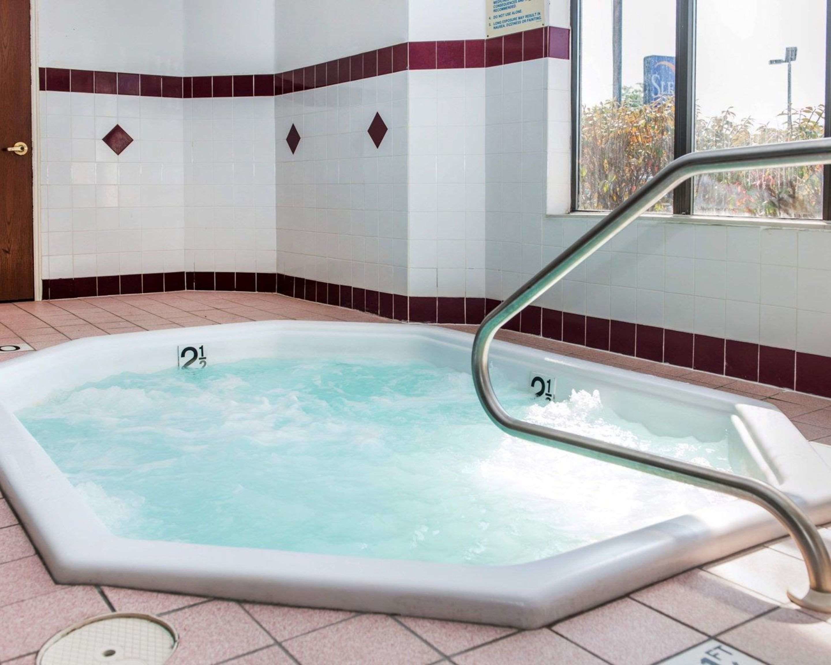 A hot tub with a metal safety rail, surrounded by tiled walls with a maroon border and diamond-shaped accents.
