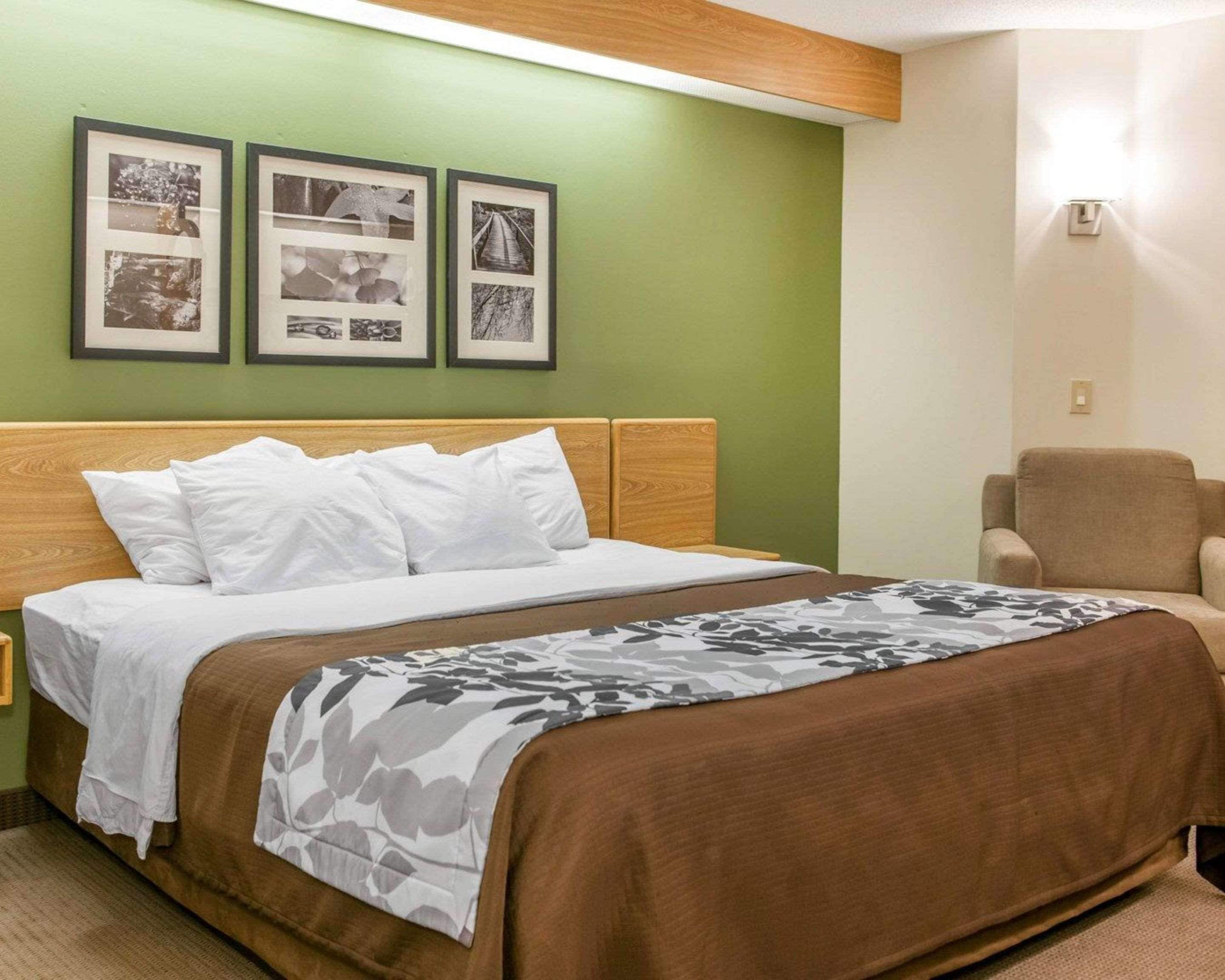 A hotel room with a bed, a chair, and three framed pictures on the wall.