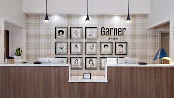 A reception desk with framed artwork on the wall and a sign that reads 'Garner by IHG'.