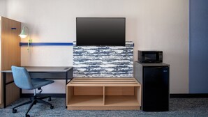 Habitación de hotel con escritorio, silla, televisor, microondas y un refrigerador pequeño.