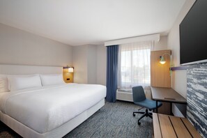 A hotel room with a large bed, a desk, a chair, a desk lamp, and a window with curtains.
