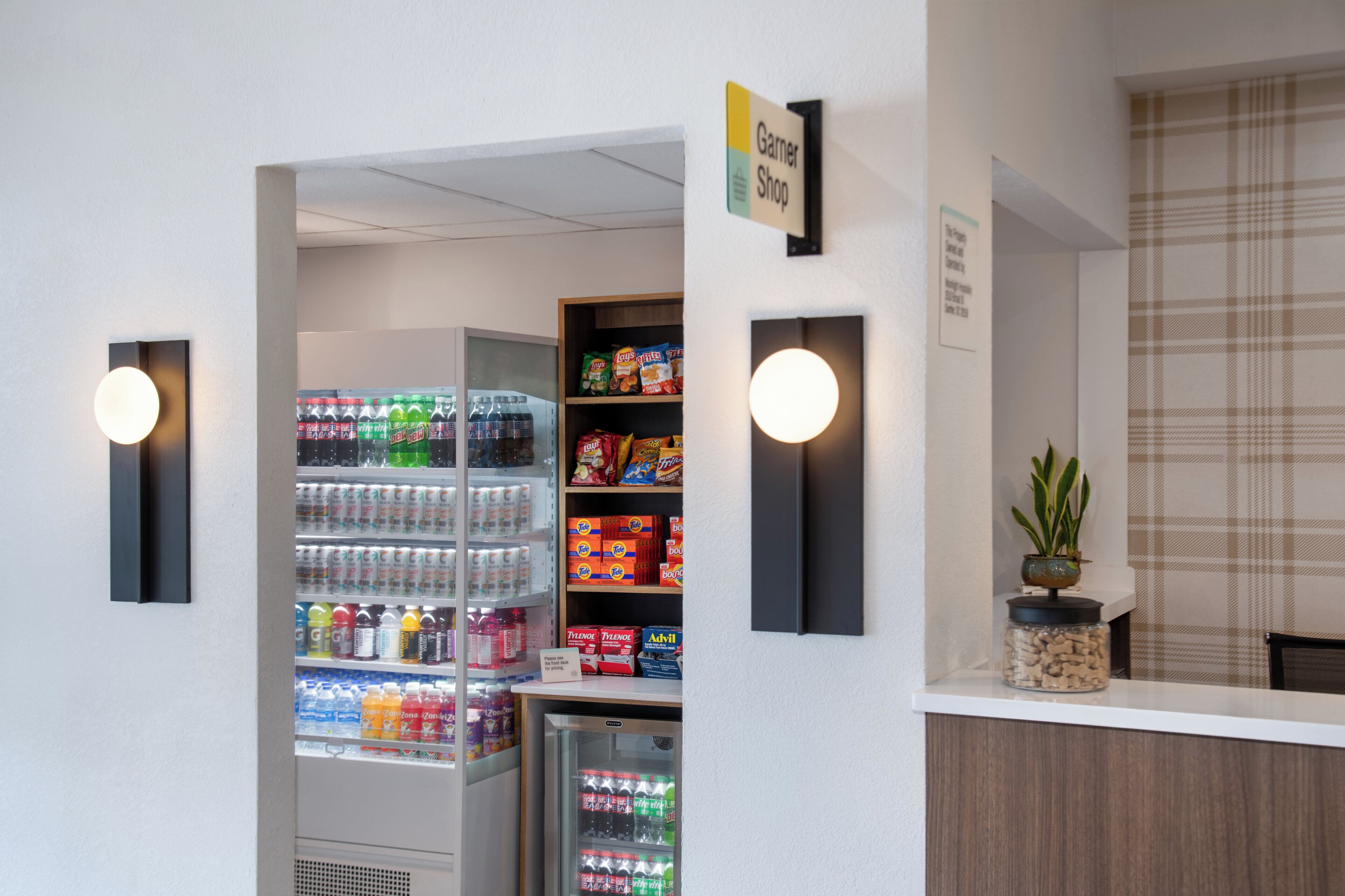 A reception area with a counter, a refrigerator stocked with beverages, and shelves with snacks and toiletries.