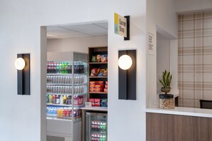 Aula, jossa on vastaanottotiski, juomia sisältävä jääkaappi sekä hyllyjä, joilla on tarjolla pientä purtavaa ja hygieniatuotteita.