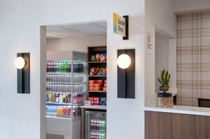 Uma área de recepção com balcão, um refrigerador cheio de bebidas e prateleiras com lanches e artigos de higiene pessoal.