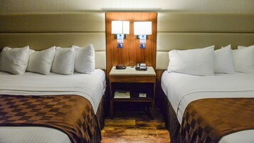 Habitación de hotel con dos camas, una mesita de noche con reloj y teléfono, y cabecero de madera.