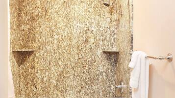 Un baño con pared de ducha de granito, una toalla blanca colgada en un perchero y un cabezal de ducha visible.