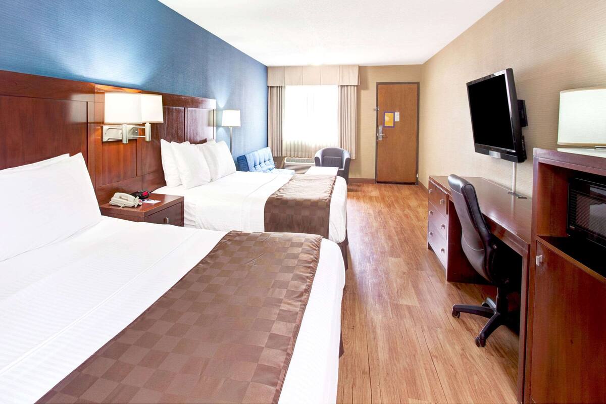 A hotel room with two beds, a desk with a TV, and a chair.