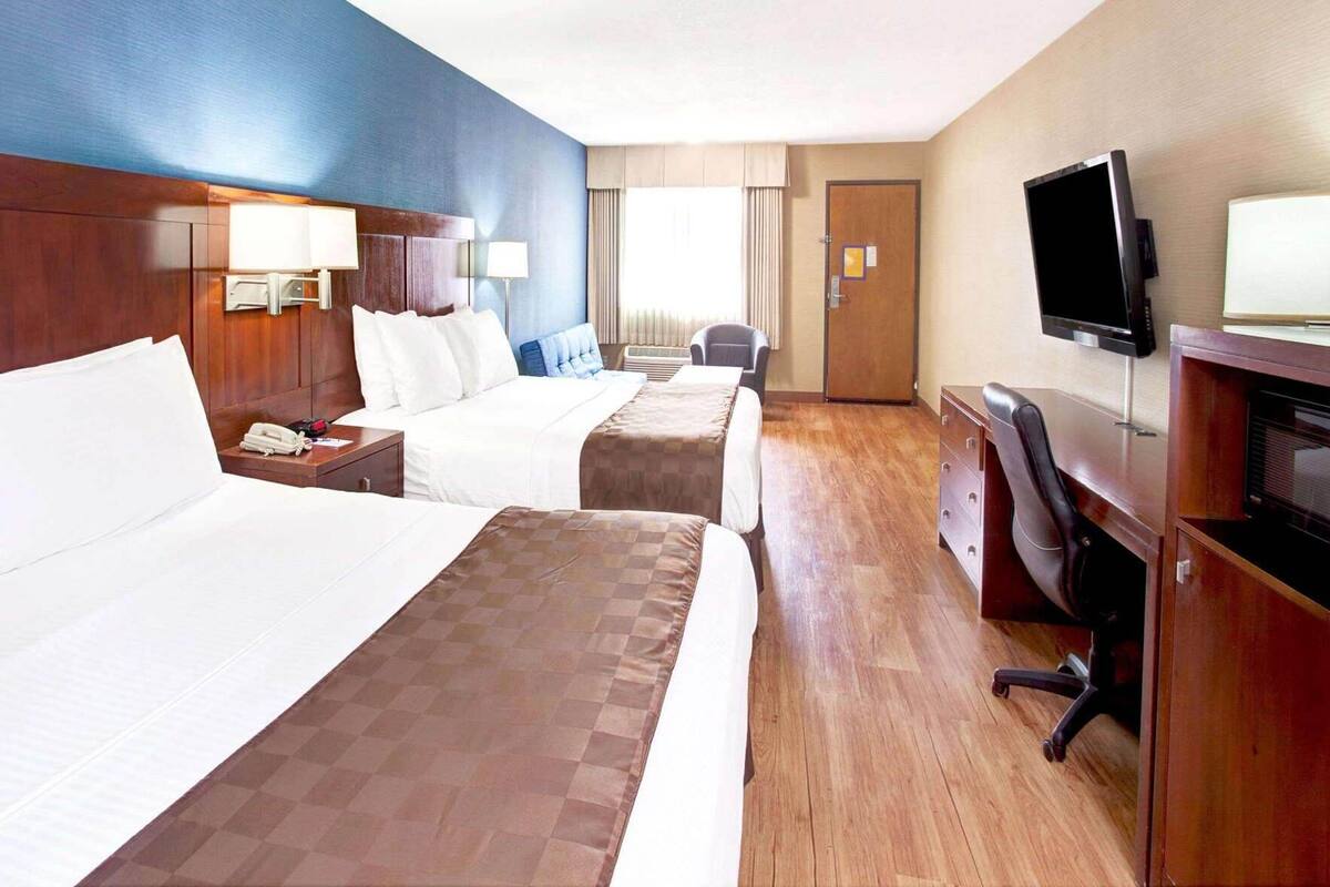 A hotel room with two beds, a desk with a chair, a television, and a window with curtains.