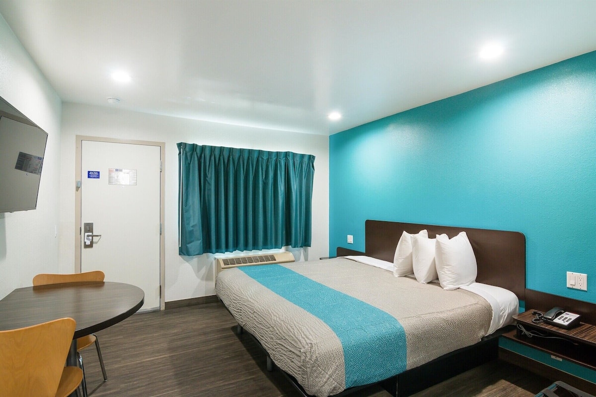Une chambre d’hôtel avec un lit, un bureau, une chaise, une télévision et une fenêtre avec des rideaux.