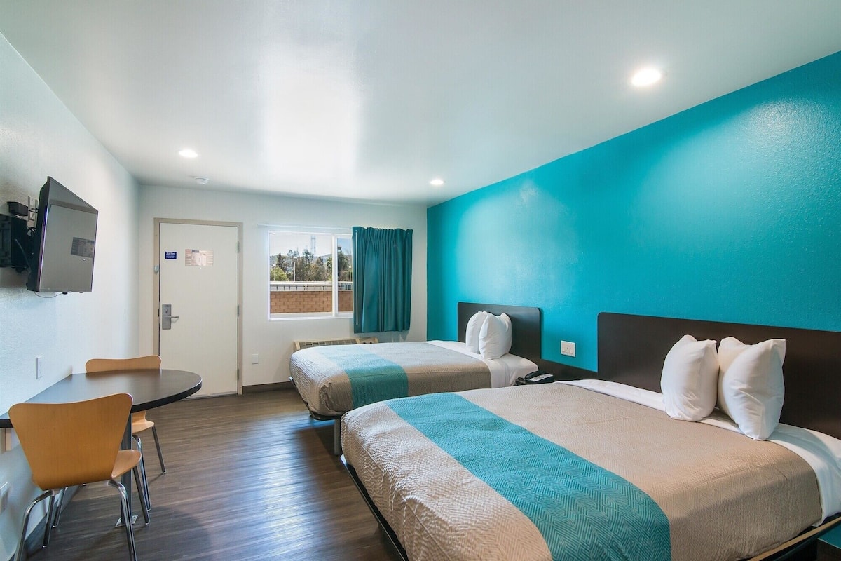 Une chambre d’hôtel avec deux lits, un bureau, une chaise et un téléviseur.