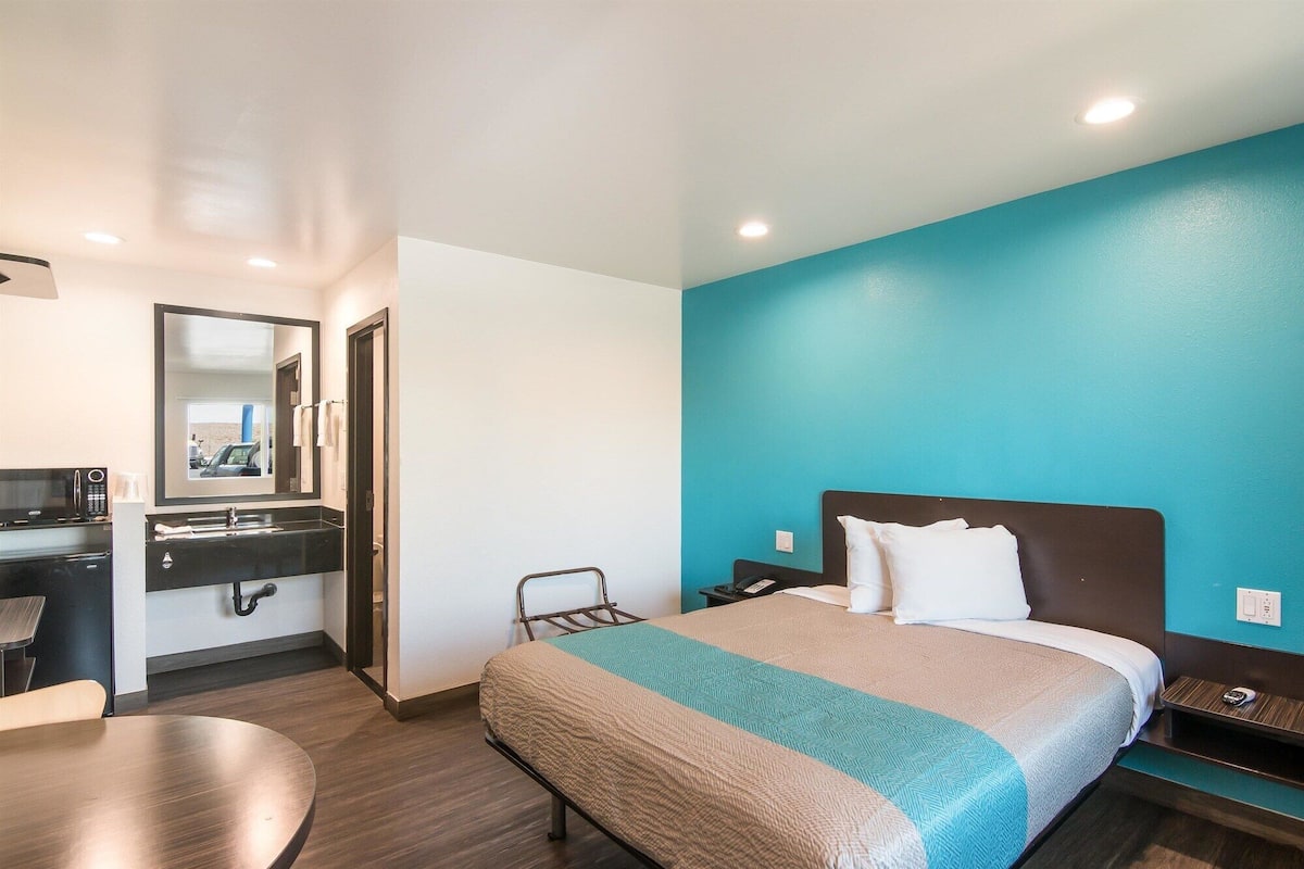 Une chambre d’hôtel comprenant un lit, un bureau avec un ordinateur, une chaise et une salle de bain avec un lavabo et un miroir.