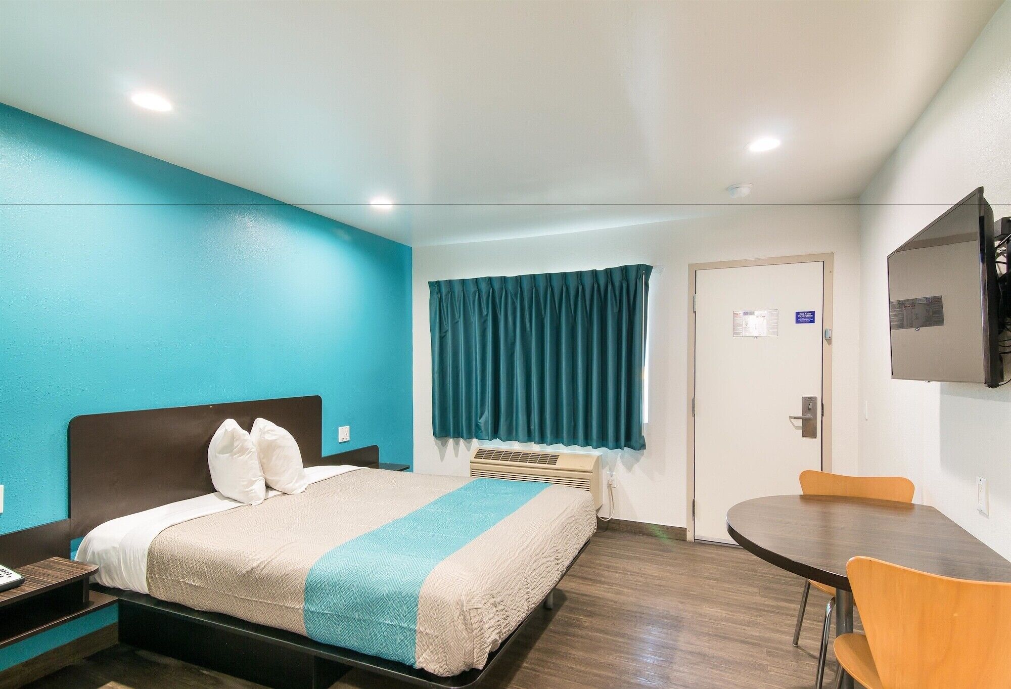 Habitación de hotel con cama, escritorio, silla, televisor y ventana con cortinas.