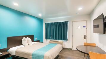Habitación de hotel con cama, escritorio, silla, televisor y ventana con cortinas.