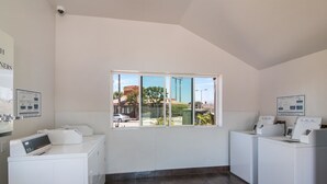 Ein Waschraum mit zwei Waschmaschinen, einem Trockner und einem Fenster mit Blick auf ein Restaurant und Bäume.