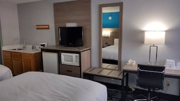 Habitación de hotel con cama, escritorio con lámpara, televisión, microondas, refrigerador pequeño y espejo.