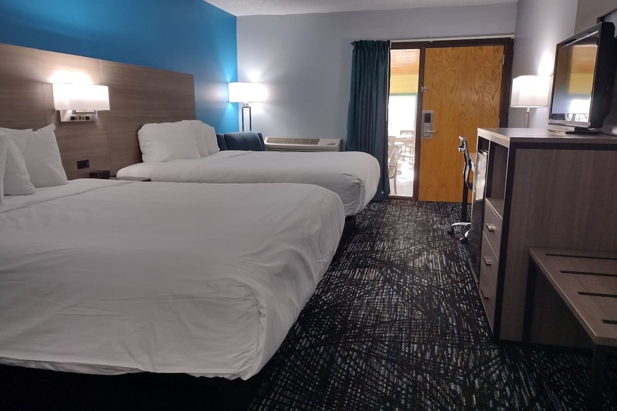 Ein Hotelzimmer mit zwei Betten, einem Schreibtisch, einem Stuhl, einem Fernseher und einer Tür, die auf einen Balkon führt.