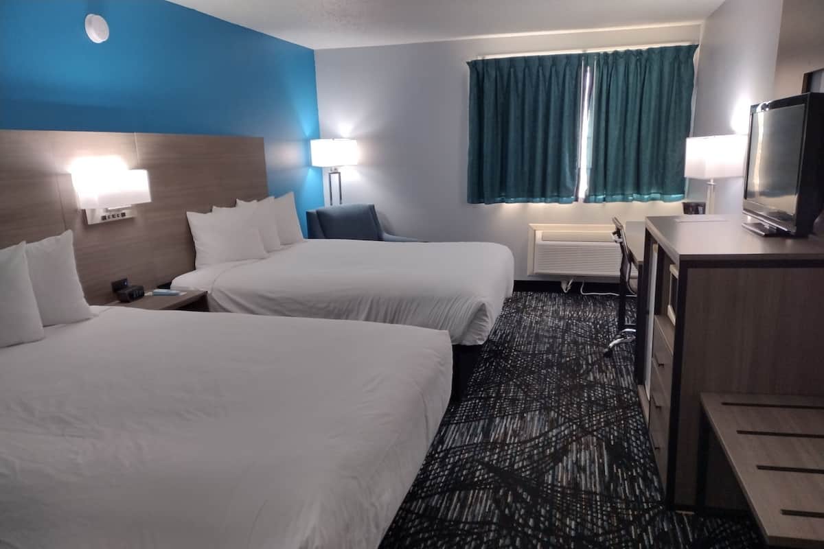 Ein Hotelzimmer mit zwei Betten, einem Schreibtisch, einem Fernseher und einem Fenster mit Vorhängen.