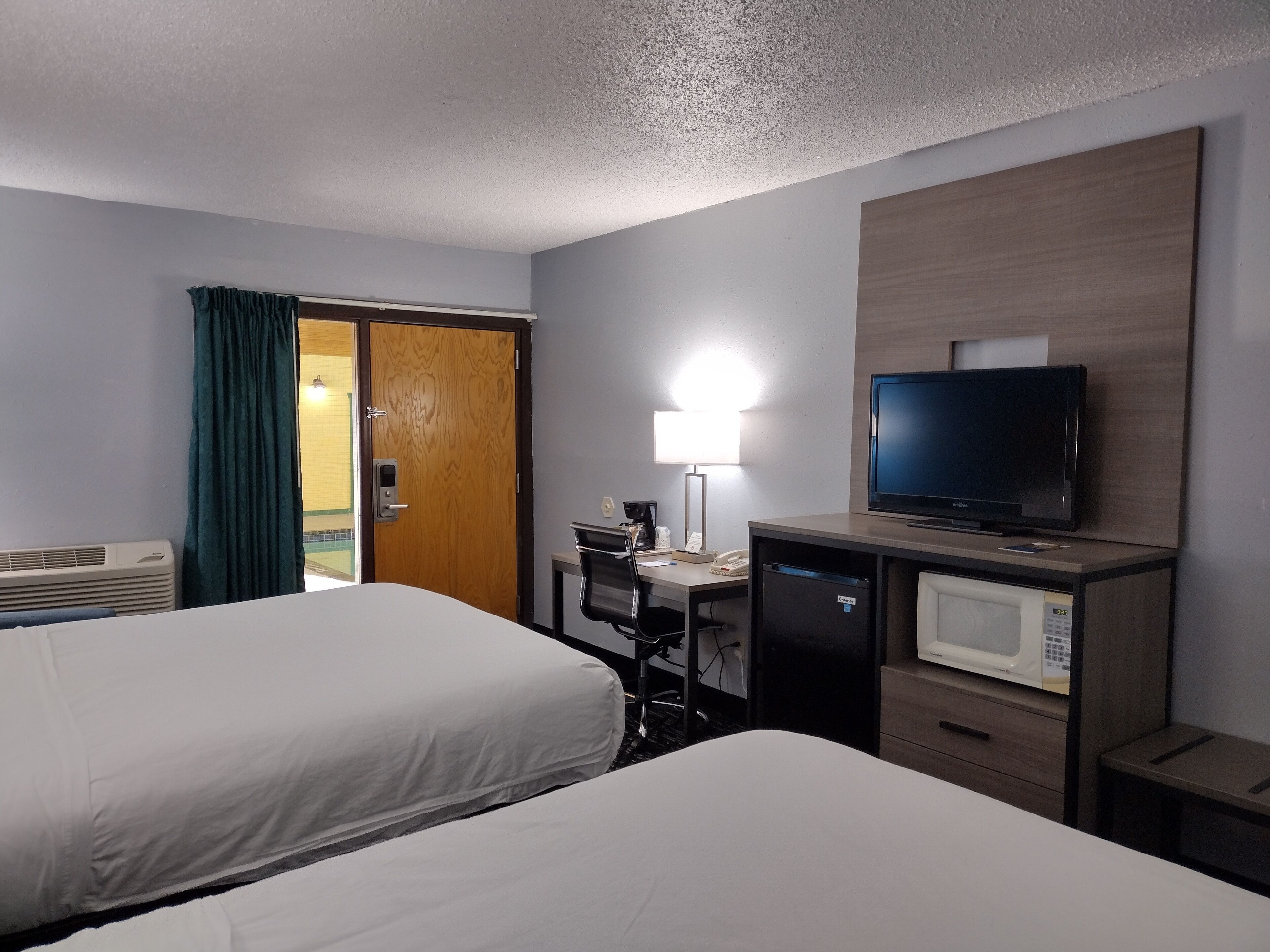 Habitación de hotel con dos camas, un escritorio con computadora, televisor, microondas y puerta que da a un balcón.