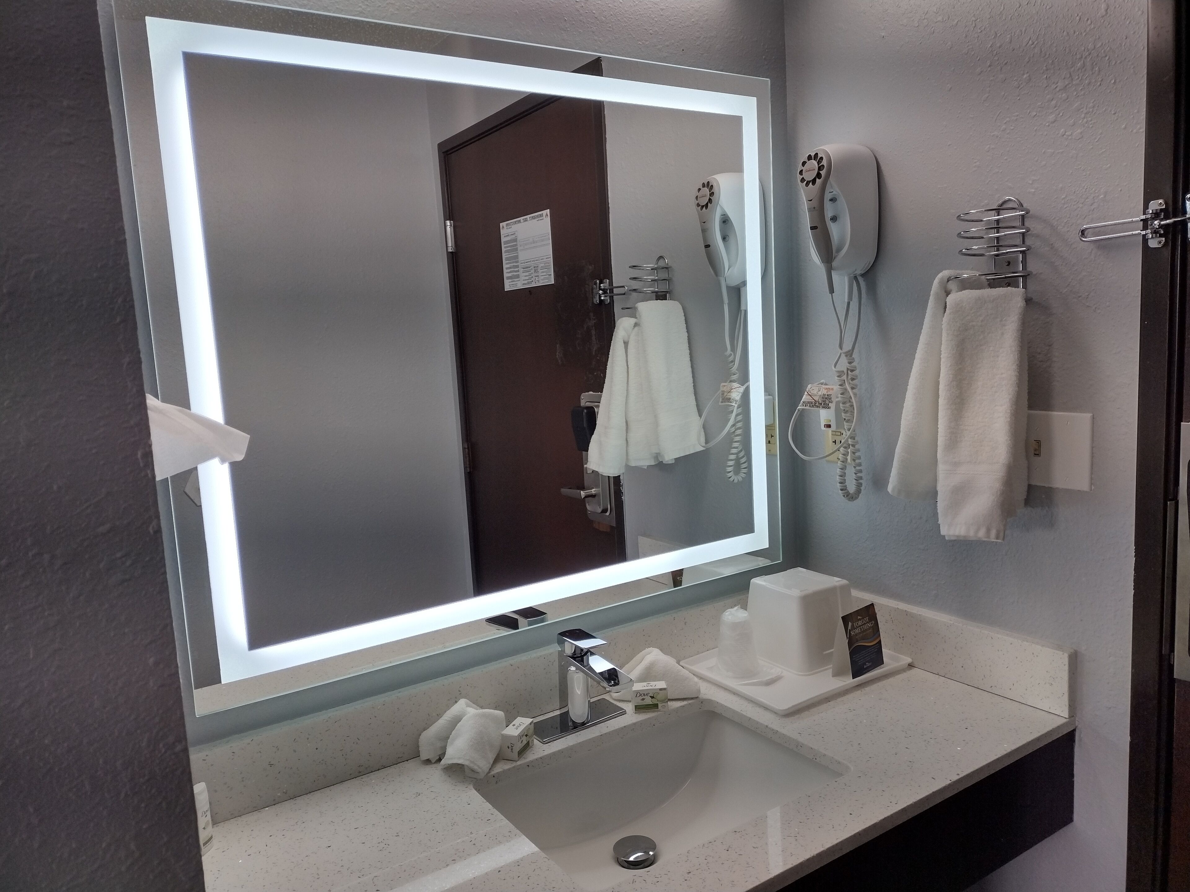 A bathroom with a large mirror, a sink, a hairdryer, and a towel rack.