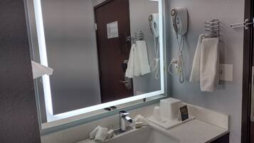 Casa de banho com um espelho grande, uma pia, um secador de cabelo e um porta-toalhas.