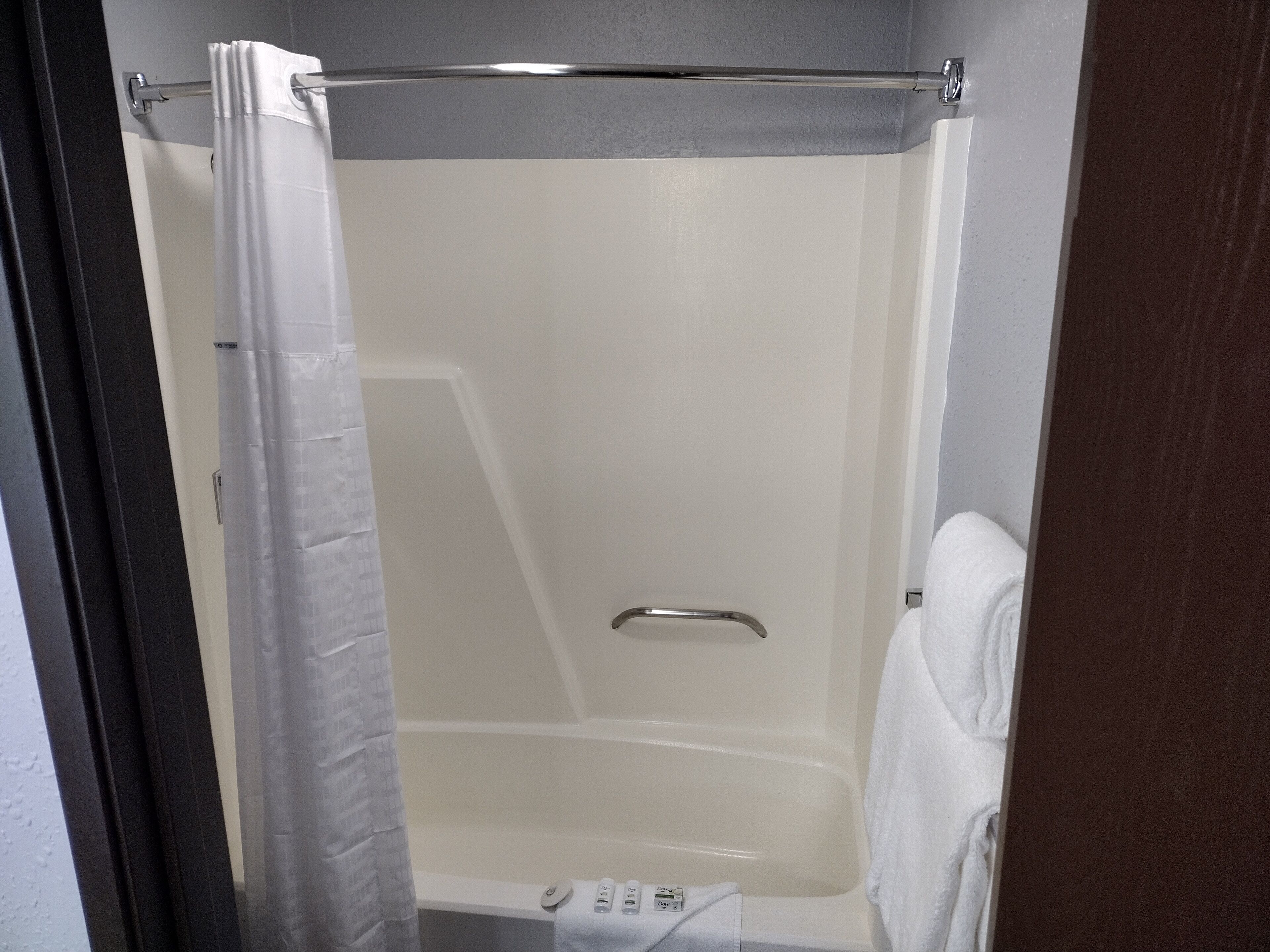 A shower with a white curtain, a handheld showerhead, and a towel rack.