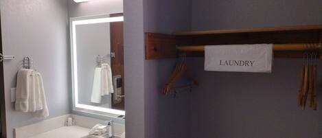 Une salle de bain avec un lavabo blanc, un miroir et un porte-serviettes. Au-dessus du porte-serviettes, on peut lire l’inscription « LINGERIE ».