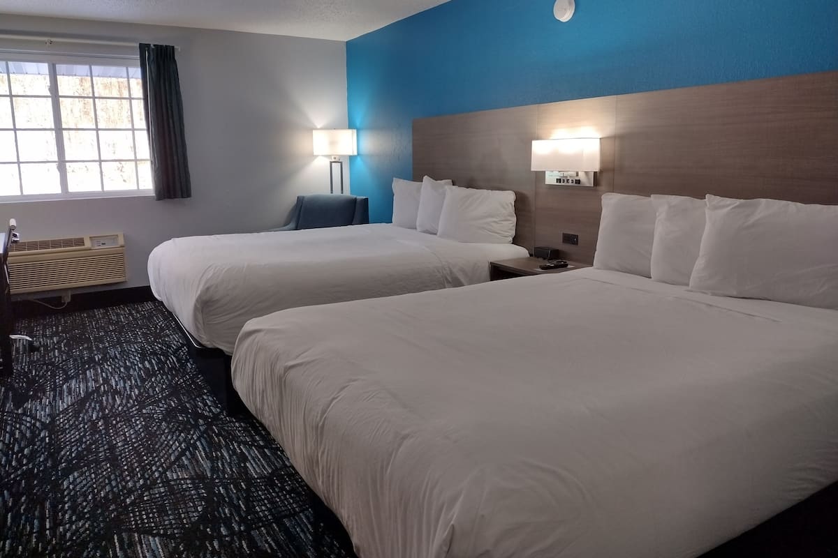 Ein Hotelzimmer mit zwei Betten, einem Schreibtisch, einem Stuhl, einer Lampe und einem Fenster mit Vorhängen.
