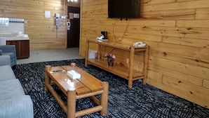 Ein Zimmer mit Holzvertäfelung, einem Holztisch, einer Couch, einem an der Wand montierten Fernseher und einem kleinen Holzregal mit einem Telefon und einer Blumenvase.