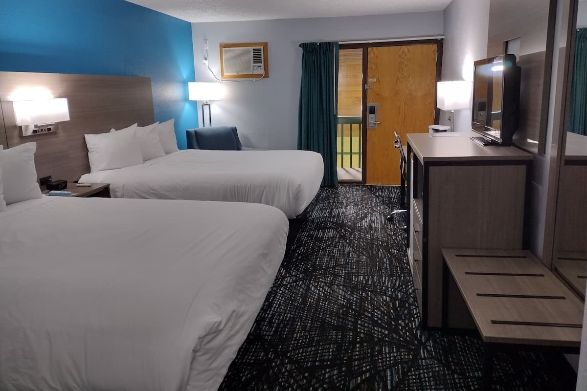Ein Hotelzimmer mit zwei Betten, einem Schreibtisch, einem Fernseher und einer Badezimmertür.