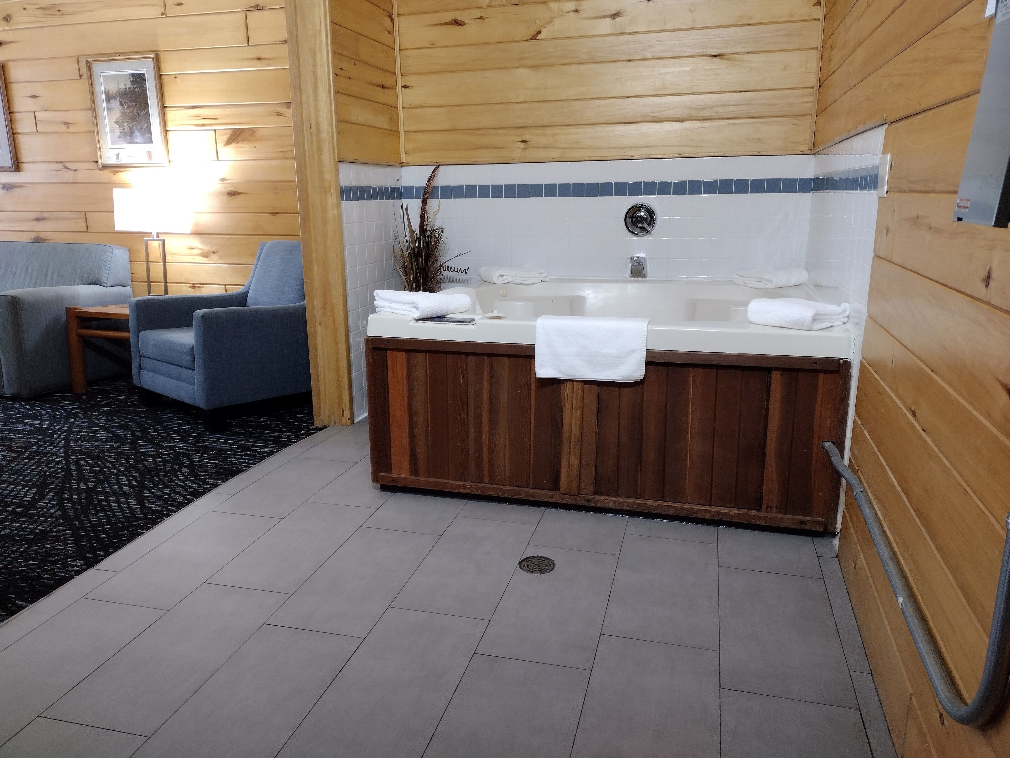 A wooden cabin interior with a wooden bathtub, two armchairs, a small table, and a tiled floor.