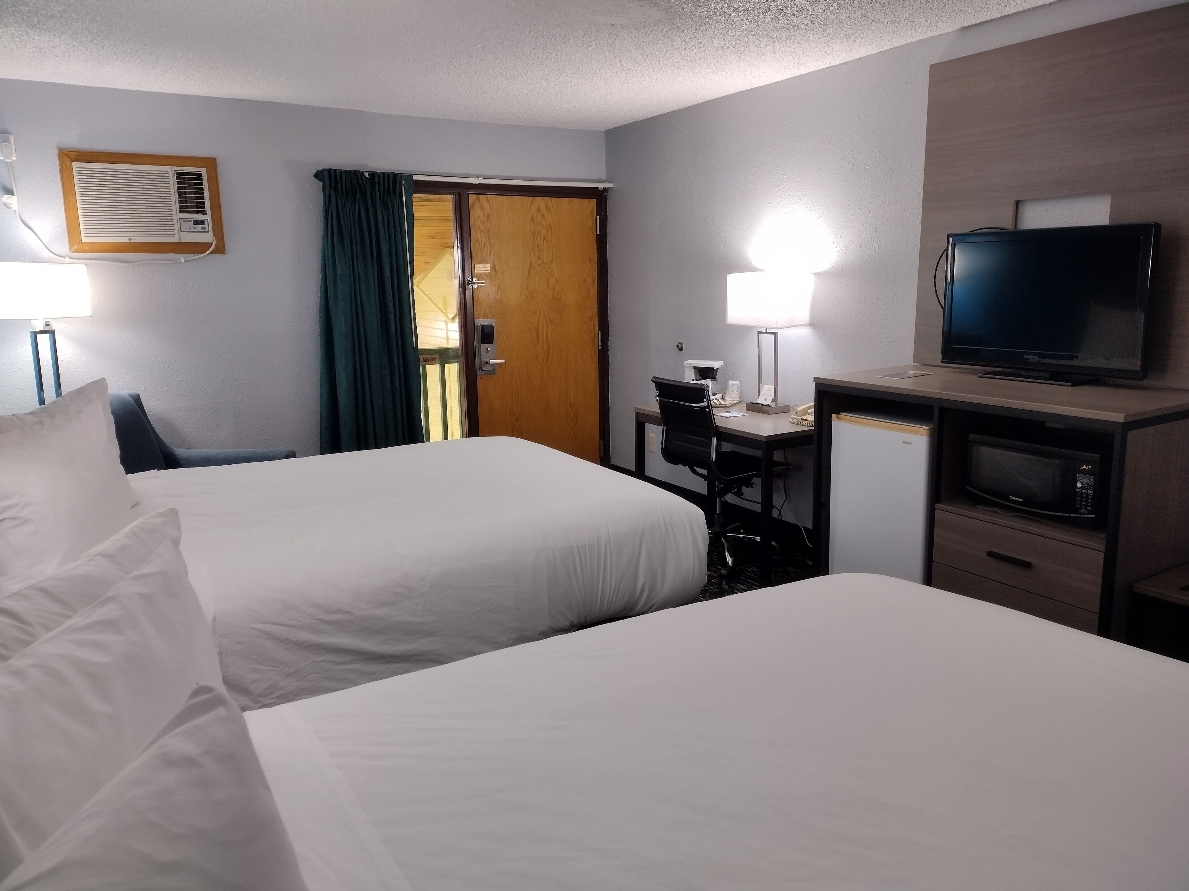 A hotel room with two beds, a desk with a computer, a TV, and a microwave.