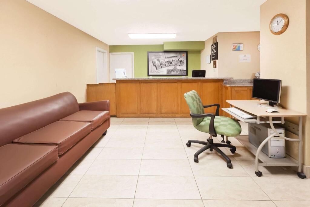 A reception area with a brown sofa, a green office chair, a desk with a computer, and a clock on the wall.
