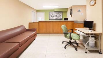 A reception area with a brown sofa, a green office chair, a desk with a computer, and a clock on the wall.