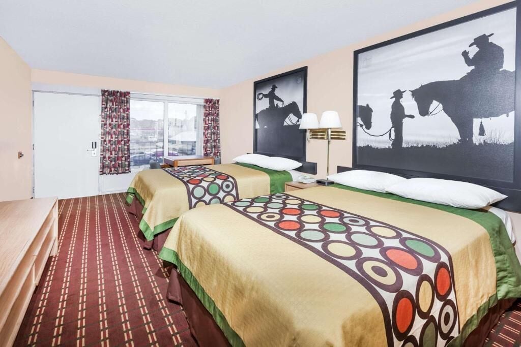 A hotel room with two beds, a window with curtains, and two wall-mounted lamps.