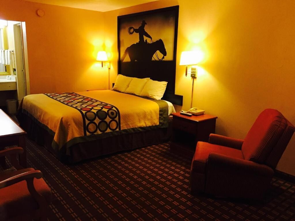 A hotel room with a bed, a chair, a nightstand, and a wall-mounted lamp.