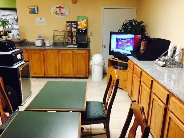 A kitchen area with a coffee machine, a television, and a sign for 'Superstart breakfast'. - Arya Inn & Extended Stay (Longview)