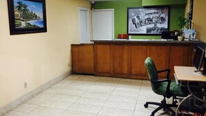 A reception area with a wooden desk, a green office chair, a framed picture on the wall, and a poster.