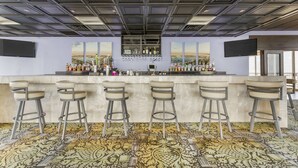 A bar area with a patterned floor, a counter with bottles, and bar stools. - Best Western Corpus Christi (Corpus Christi)